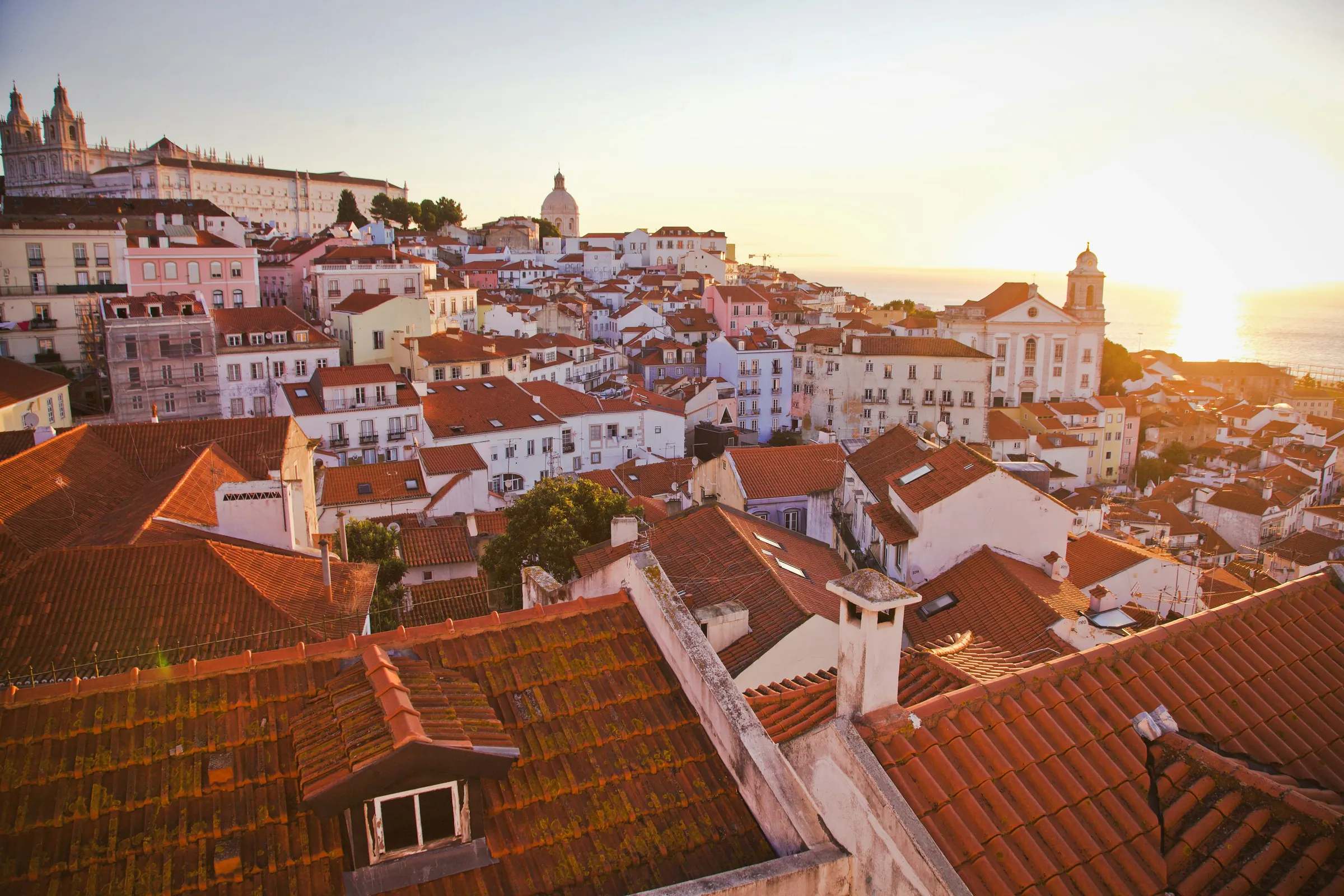Sunlit terracotta rooftops of Lisbon at sunrise, the sun low over the river